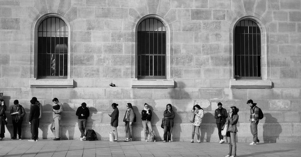 Black and white photo showing a group of people waiting outside a historic stone building with arched windows.